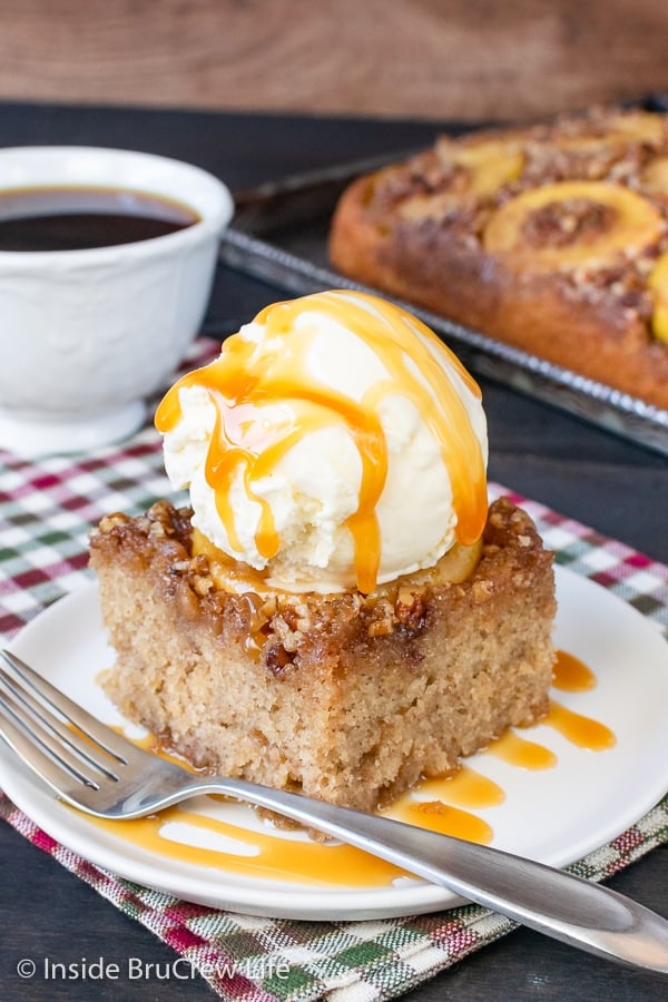 A white plate with a slice of apple upside down cake with a scoop of vanilla ice cream and caramel drizzles on it.