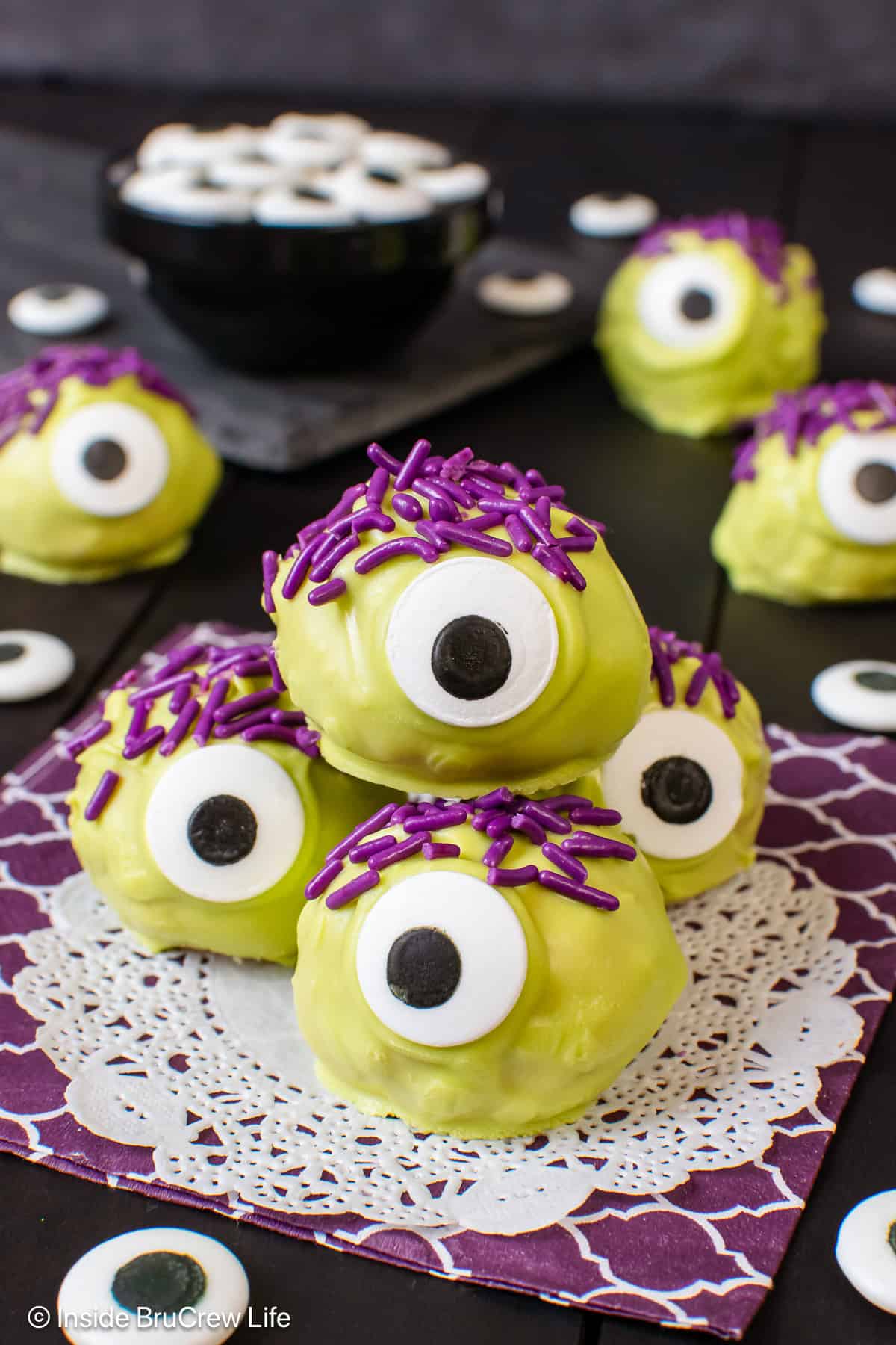 A pile of peanut butter monsters with purple sprinkle hair on a purple napkin.