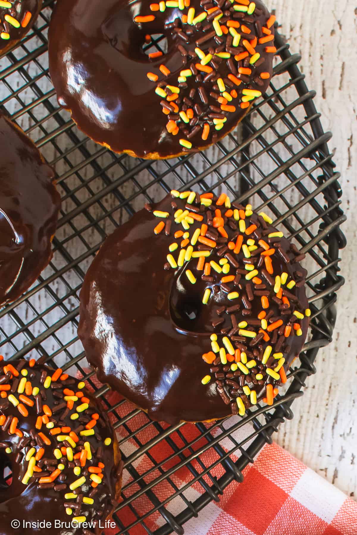 A black wire rack with chocolate glazed pumpkin donuts on it.