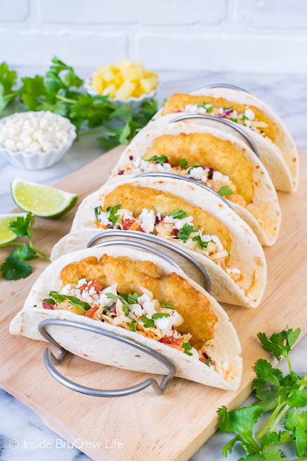 A metal taco holder with four easy fish tacos in it filled with crispy fish, slaw, and cheese