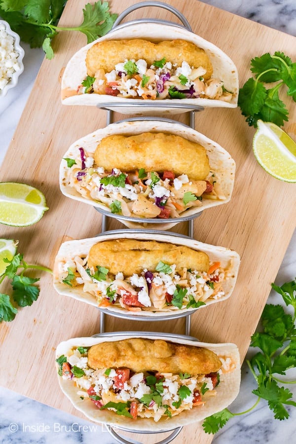 Overhead picture of a metal taco holder with four fish tacos in it with slaw, cheese, and cilantro on top