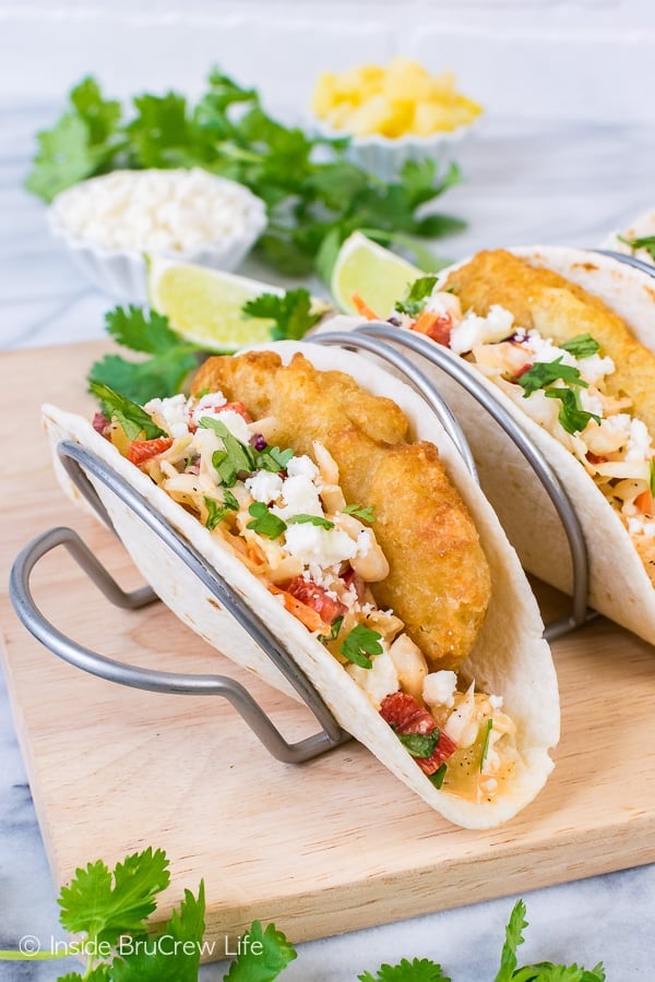 A metal taco holder with fish tacos loaded with crispy fish, slaw, and cheese in them
