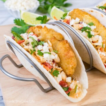 A flour tortilla in a taco stand filled with crispy fish, slaw, and cheese