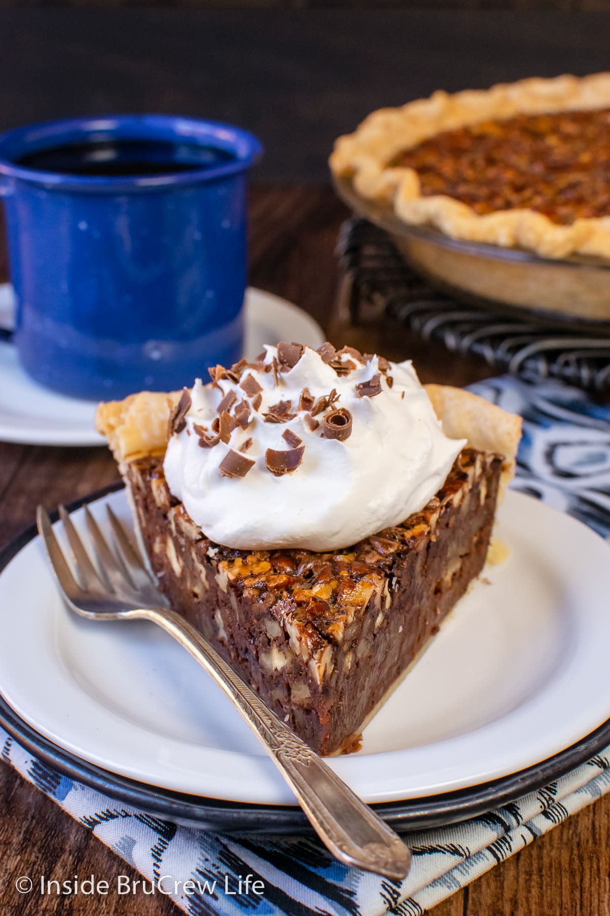 A slice of fudge pecan pie with whipped cream on a white plate.