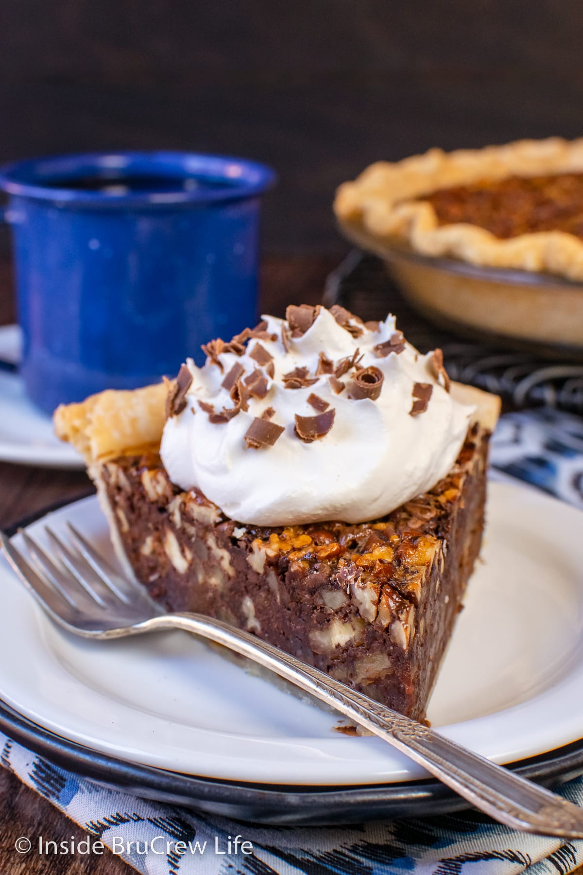 A slice of fudge pecan pie with whipped cream on a white plate.