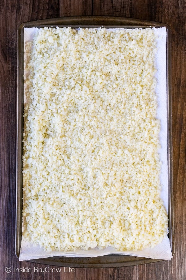 A sheet pan lined with paper towels with a batch of easy cauliflower rice on it.