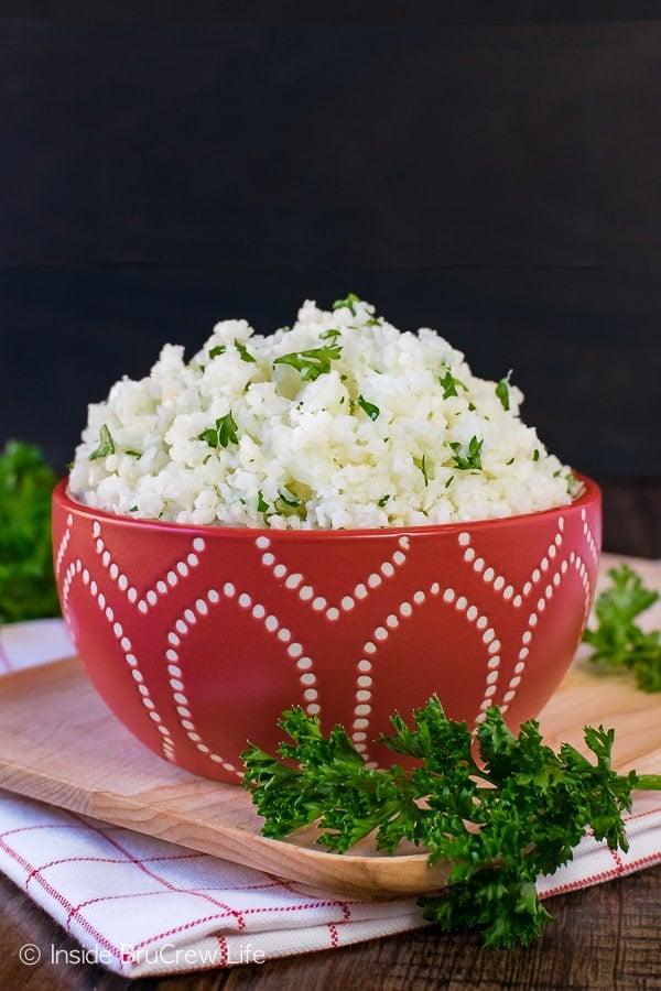 A red bowl on a wooden cutting board filled with homemade cauliflower rice.