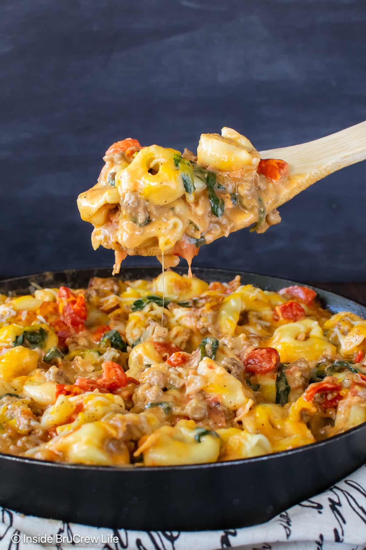 A skillet of cheeseburger tortellini with a spoon lifting some out.