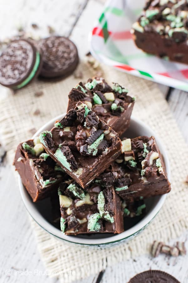 Multiple pieces of chocolate fudge loaded with green mint cookies and mint chips in a white bowl.