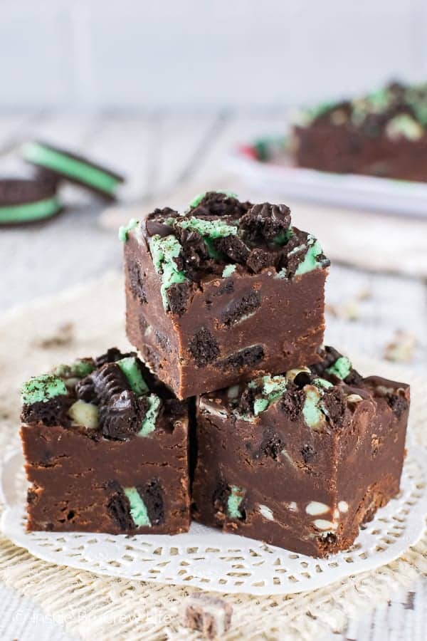 3 pieces of chocolate fudge loaded with green mint cookies and mint chips on a white doily.
