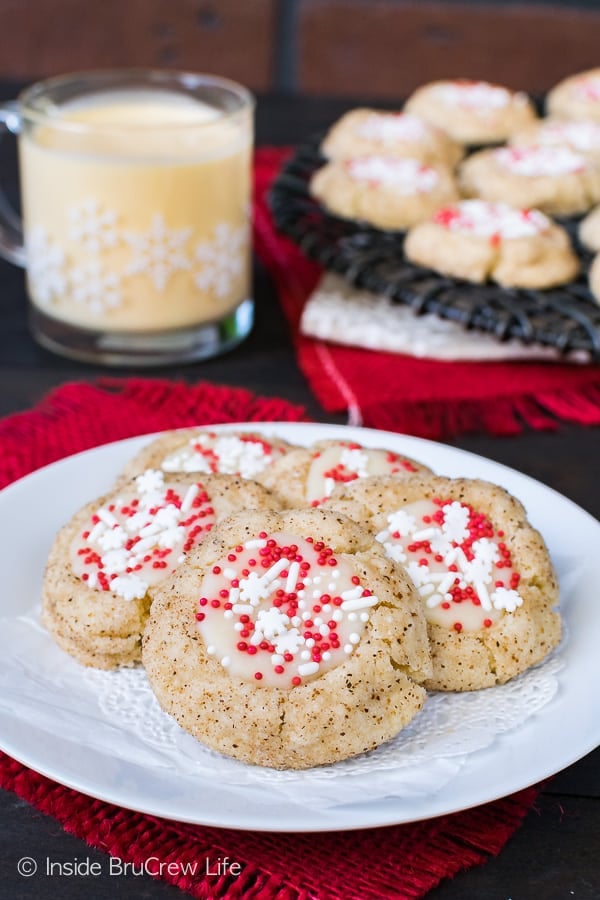 Eggnog Thumbprint cookies on a white plate with cookies and eggnog in the background.