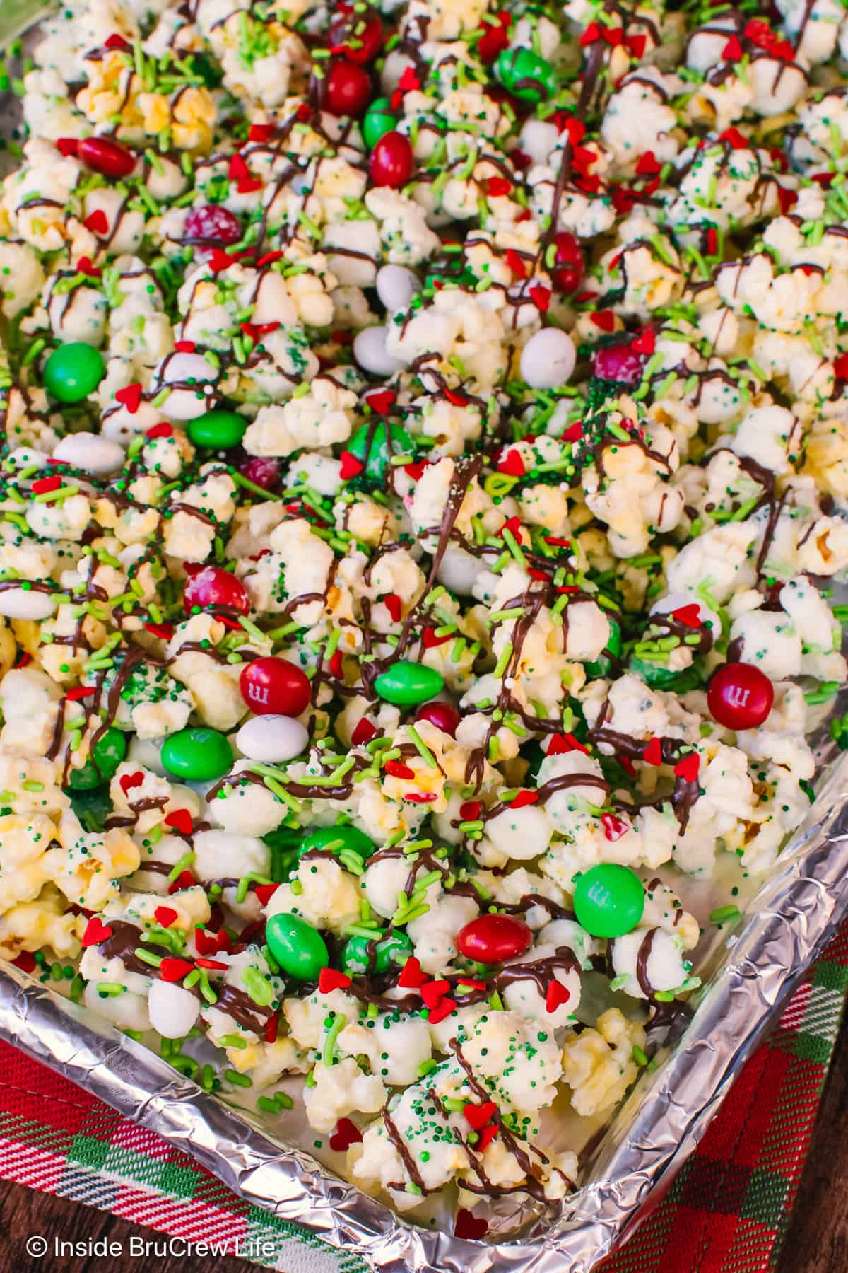 A pan of Grinch popcorn topped with chocolate drizzles, M&M's, and red sprinkle hearts.