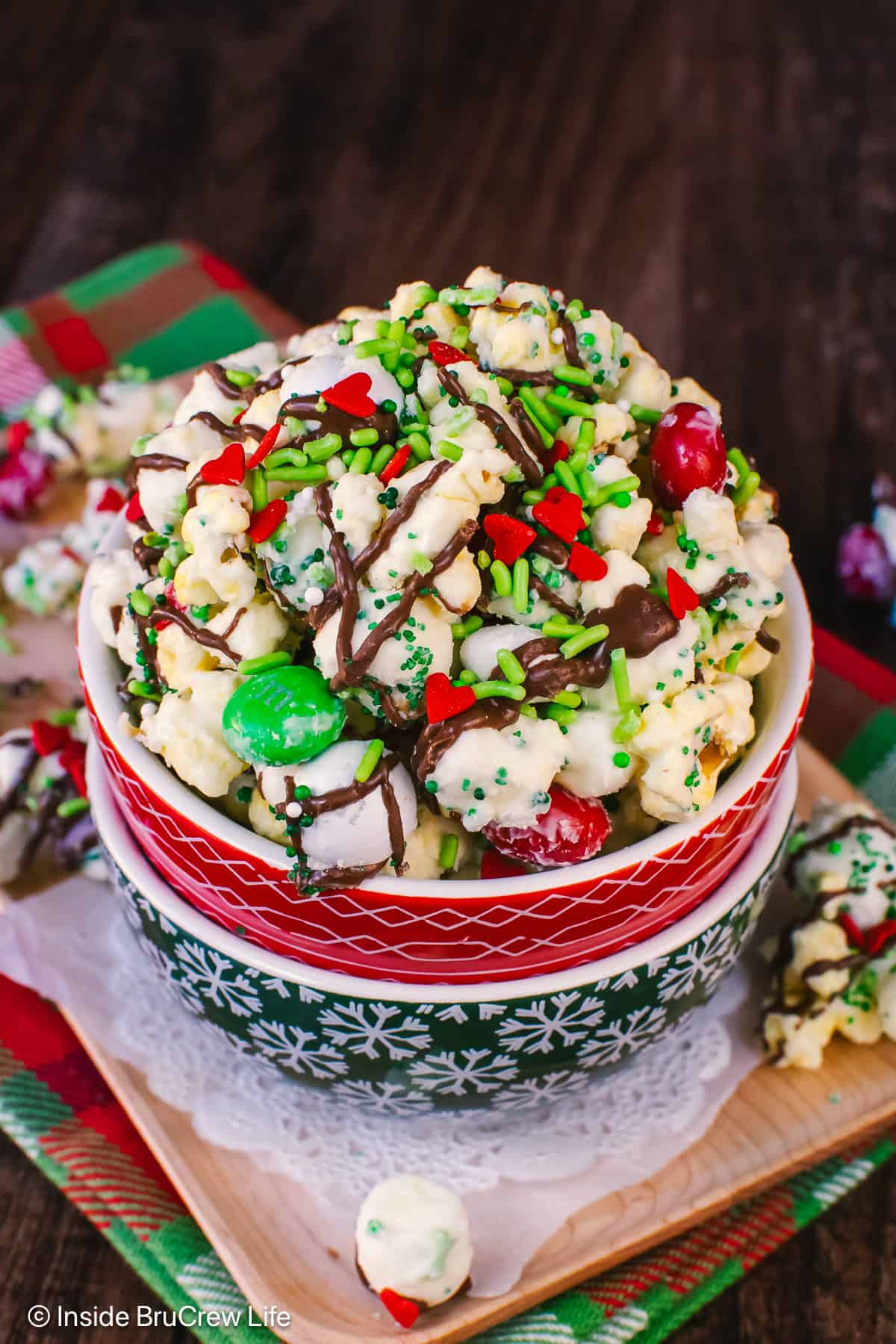 A bowls filled with a chocolate covered popcorn topped with red and green candies and sprinkles.