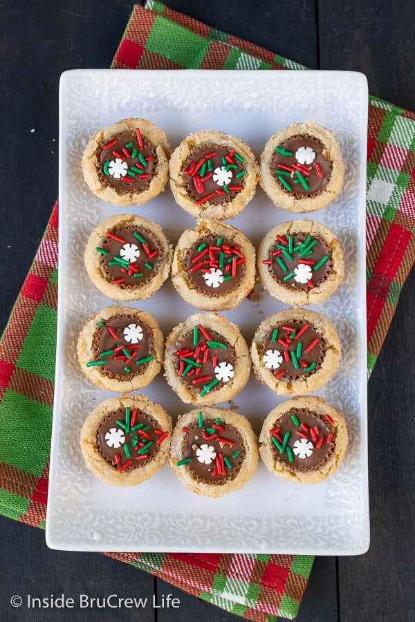 An overhead picture of a white plate with 12 peanut butter cup cookies topped with holiday sprinkles on it.
