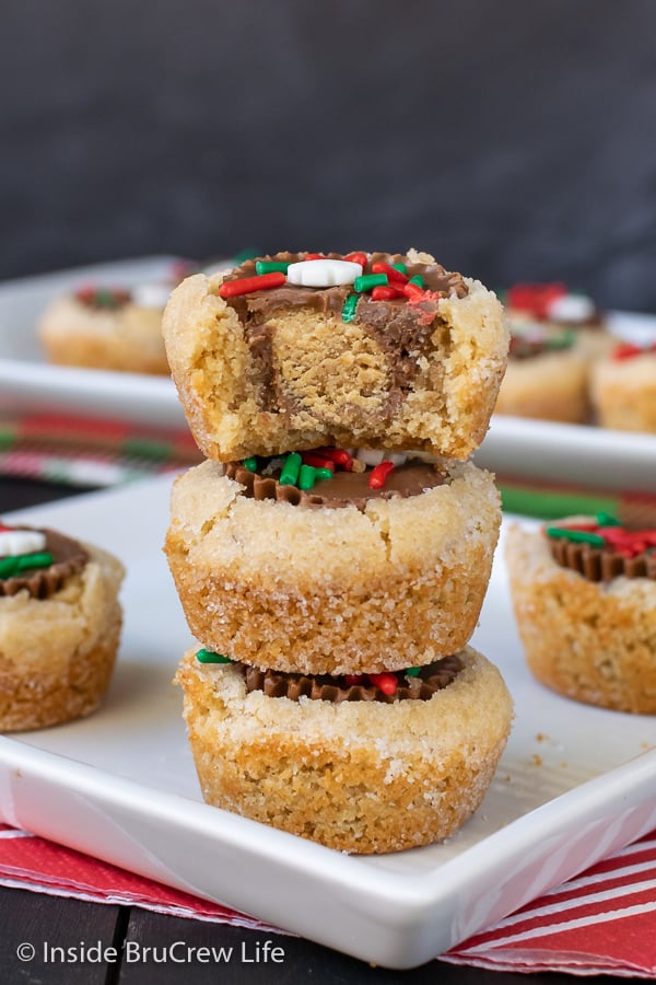 A white plate with three peanut butter cup cookies stacked on it and a bite taken out of the top cookie.