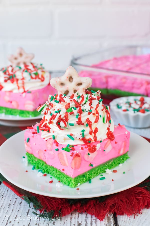 No Bake Peppermint Cheesecake Bars loaded with cool whip and red and green sprinkles on a white plate.