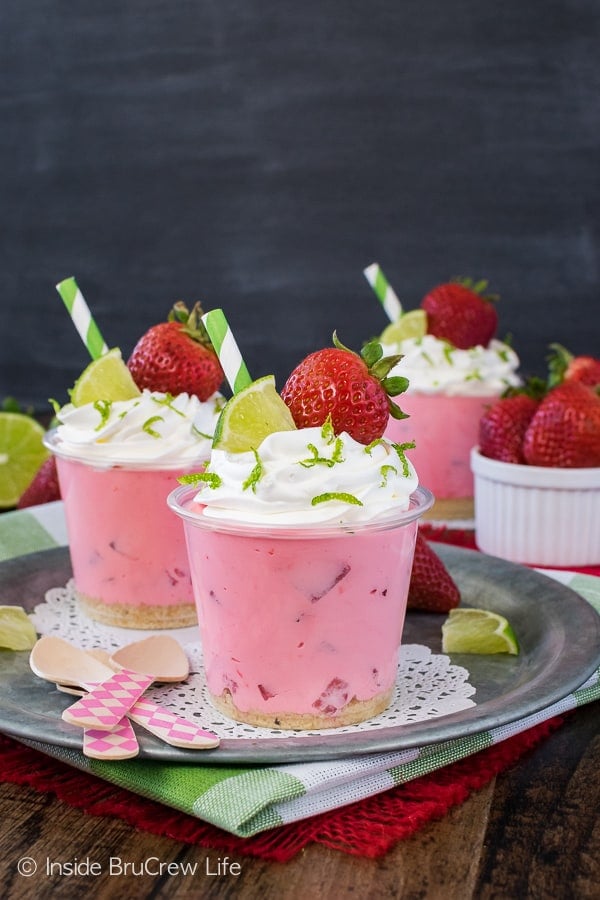 A metal tray with pink desserts topped with whipped topping and strawberries.