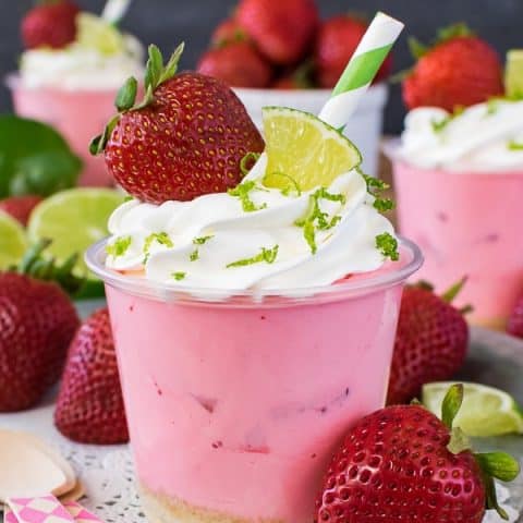 A metal tray with pink desserts topped with whipped topping and strawberries.