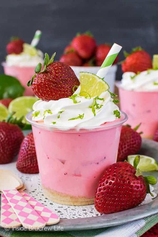A small cup with pink no bake strawberry daiquiri cheesecake in it surrounded by strawberries.
