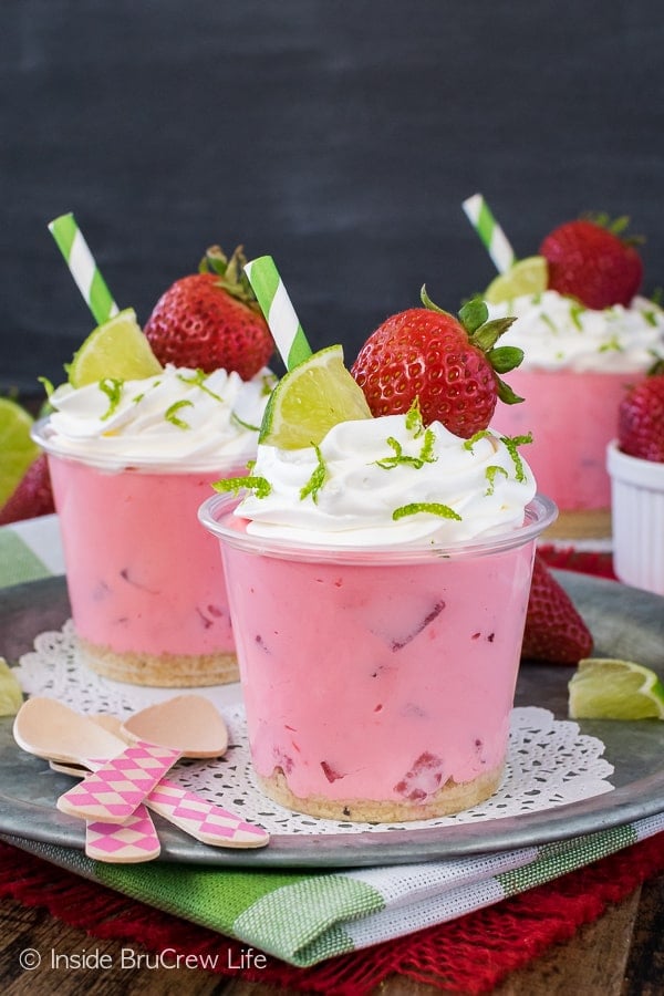 Pink desserts topped with whipped topping and strawberries on a metal tray.