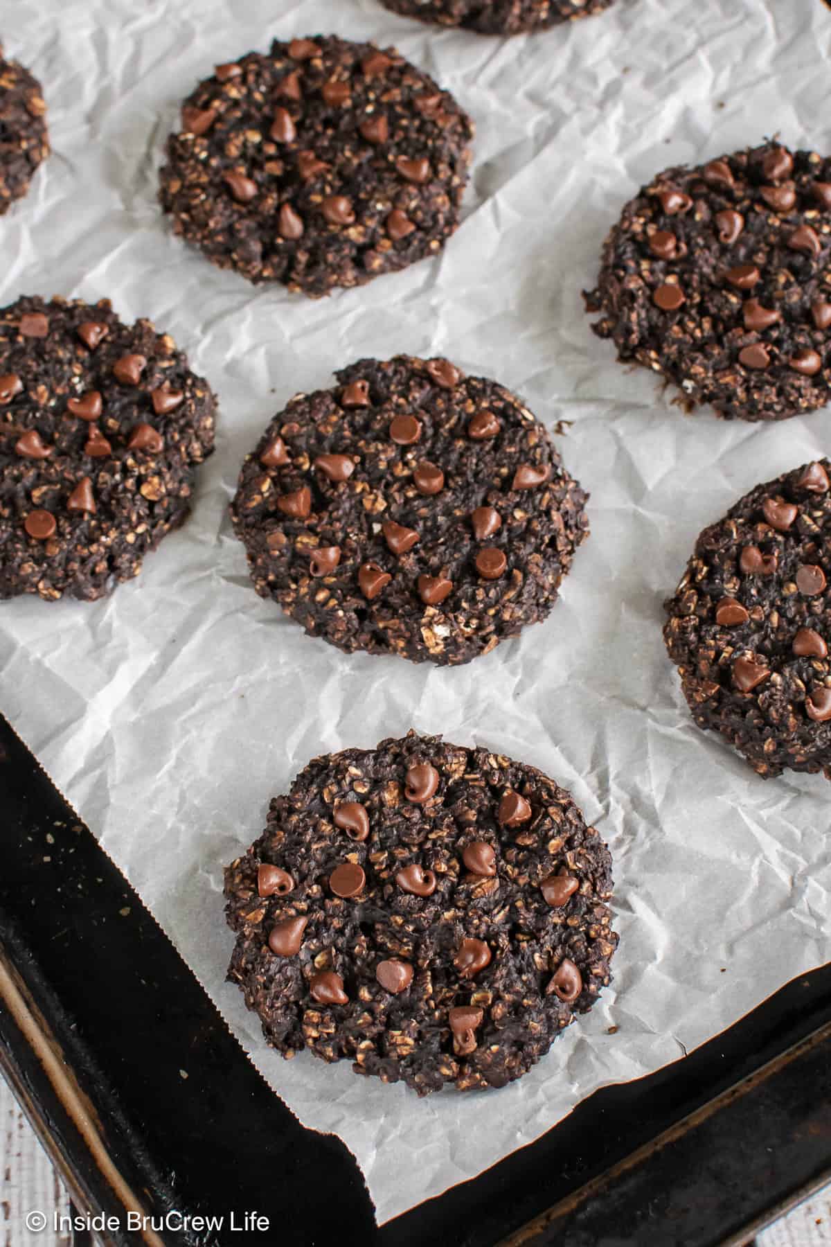 A dark sheet pan with parchment and a batch of chocolate protein cookies on it.