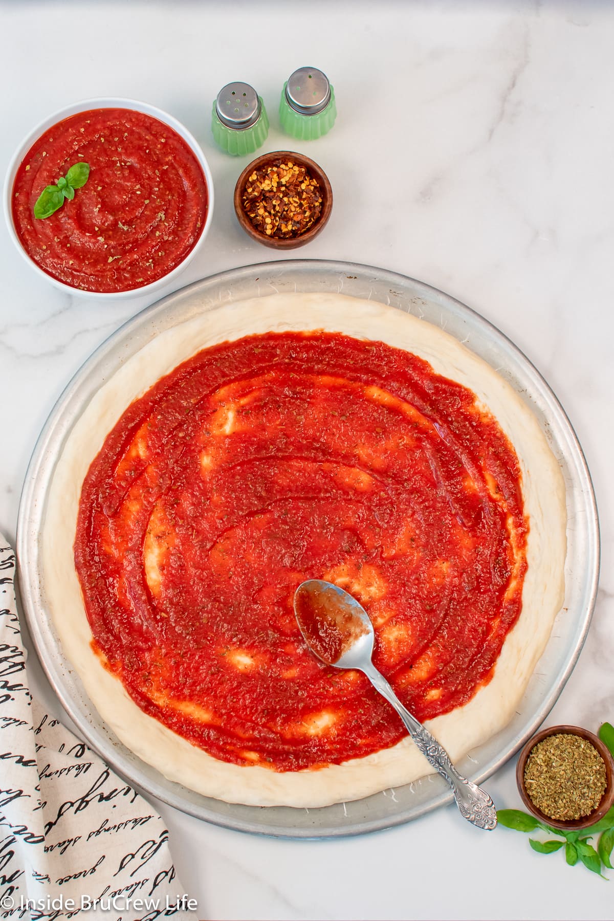 Pizza dough on a pan with sauce spread out on it.