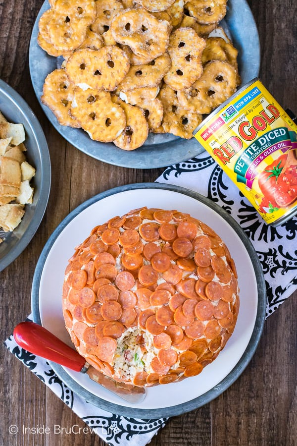 A cheese ball covered in mini pepperonis on a plate with pretzels.