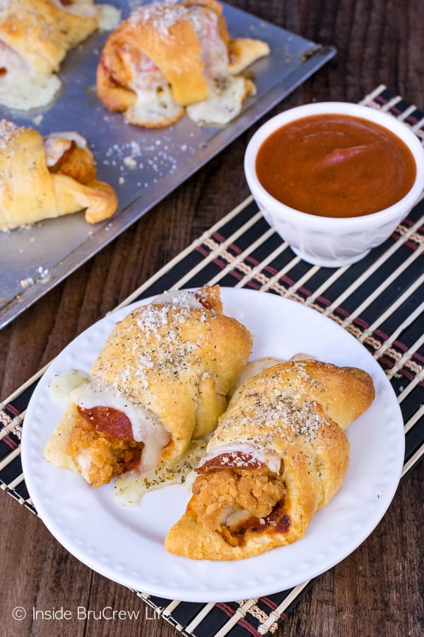 2 chicken rolls on a white plate with a bowl of pizza dipping sauce.