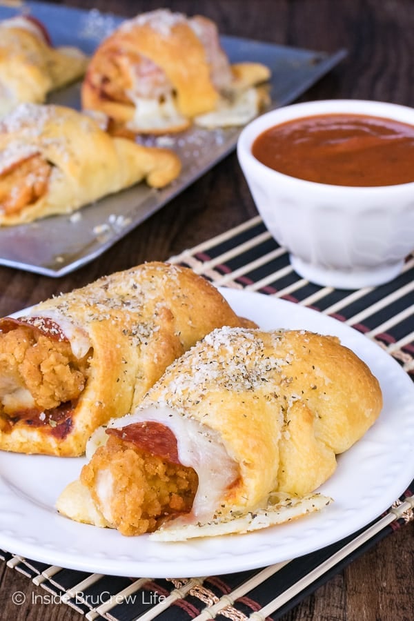 Close up picture of a crescent roll sandwich on a white plate. The roll has a chicken tender, pepperoni, and melted cheese inside it.