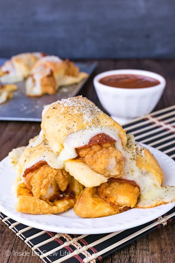 Three crescent roll sandwiches on a white plate. Each rolls has a chicken tender, mozzarella cheese, and pepperoni in it.