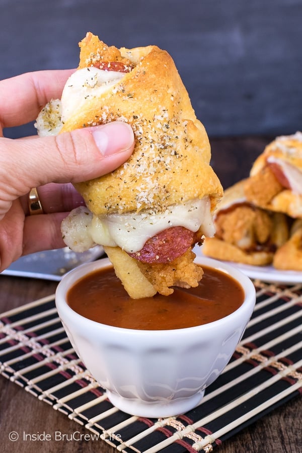 A warm crescent roll sandwich wrapped around chicken, pepperoni, and melted cheese being dipped into a white bowl of pizza sauce.