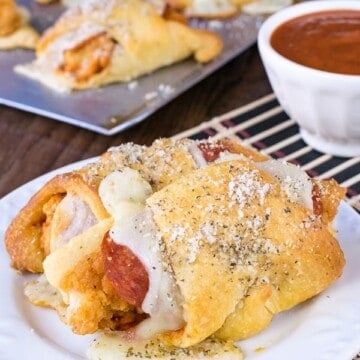 2 crescent rolls stuffed with chicken, cheese, and pizza sauce on a white plate.