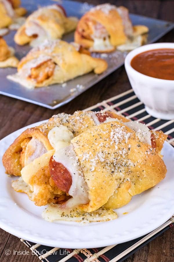 Two crescent rolls sandwiches on a white plate filled with gooey cheese, pepperoni, and chicken tenders.