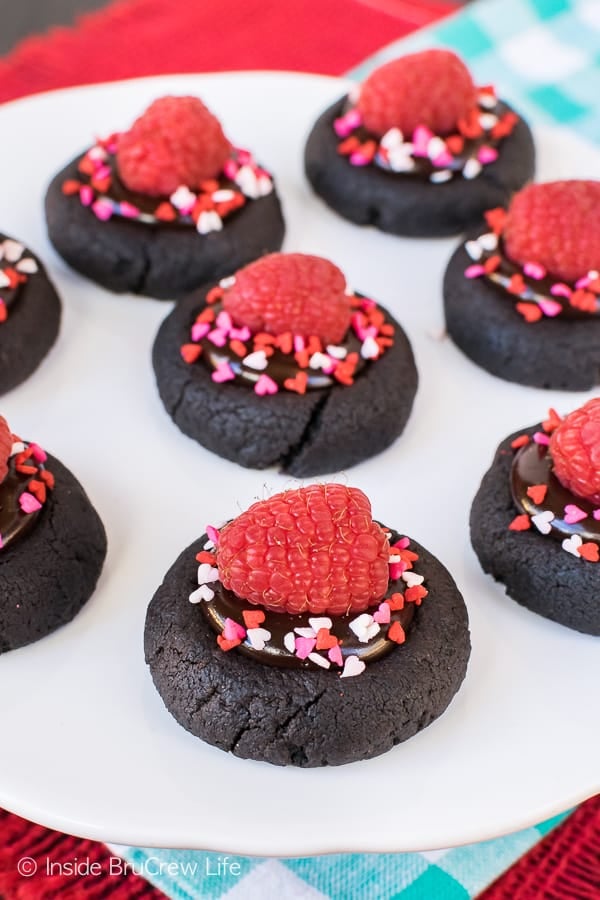 Dark chocolate cookies with dark chocolate frosting topped with sprinkles and a fresh raspberry.