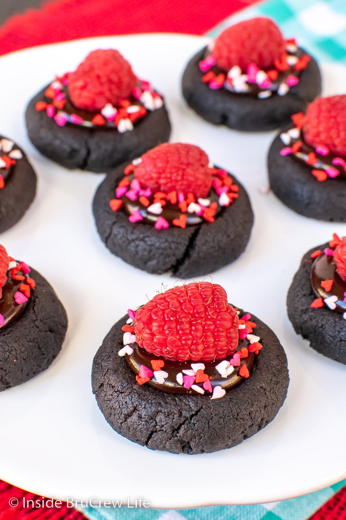 A white plate with chocolate thumbprint cookies topped with raspberries on it.