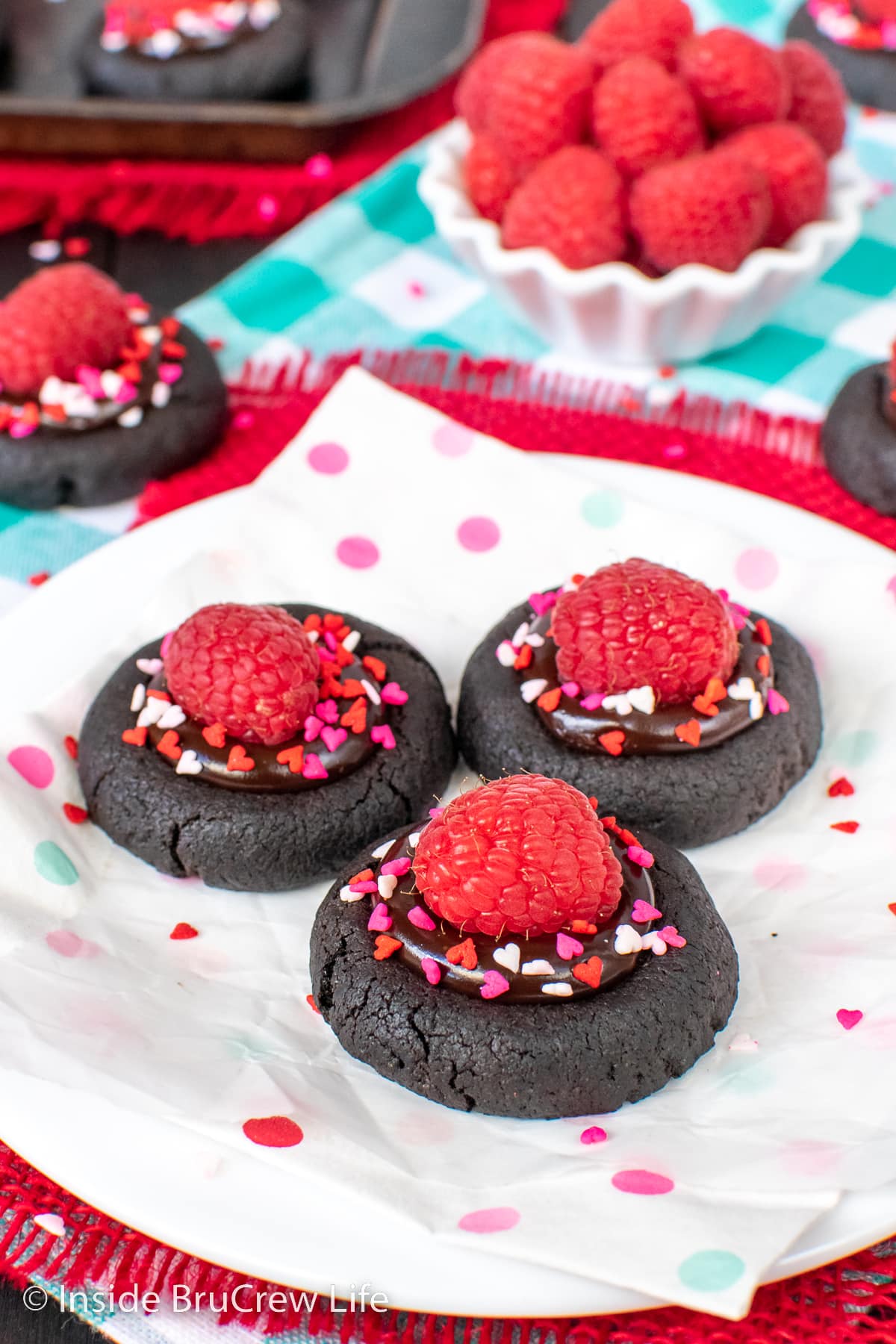 Three chocolate thumbprints topped with raspberries on a white plate.