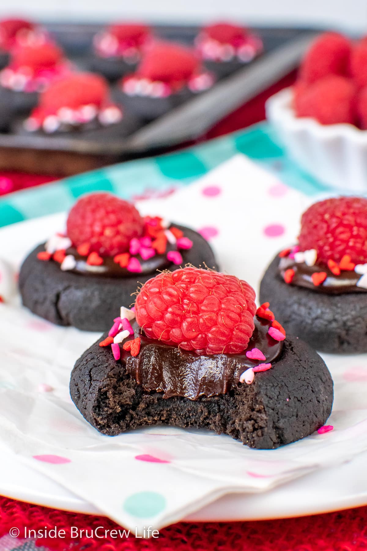 A chocolate thumbprint cookie with a chocolate center and a raspberry on it.