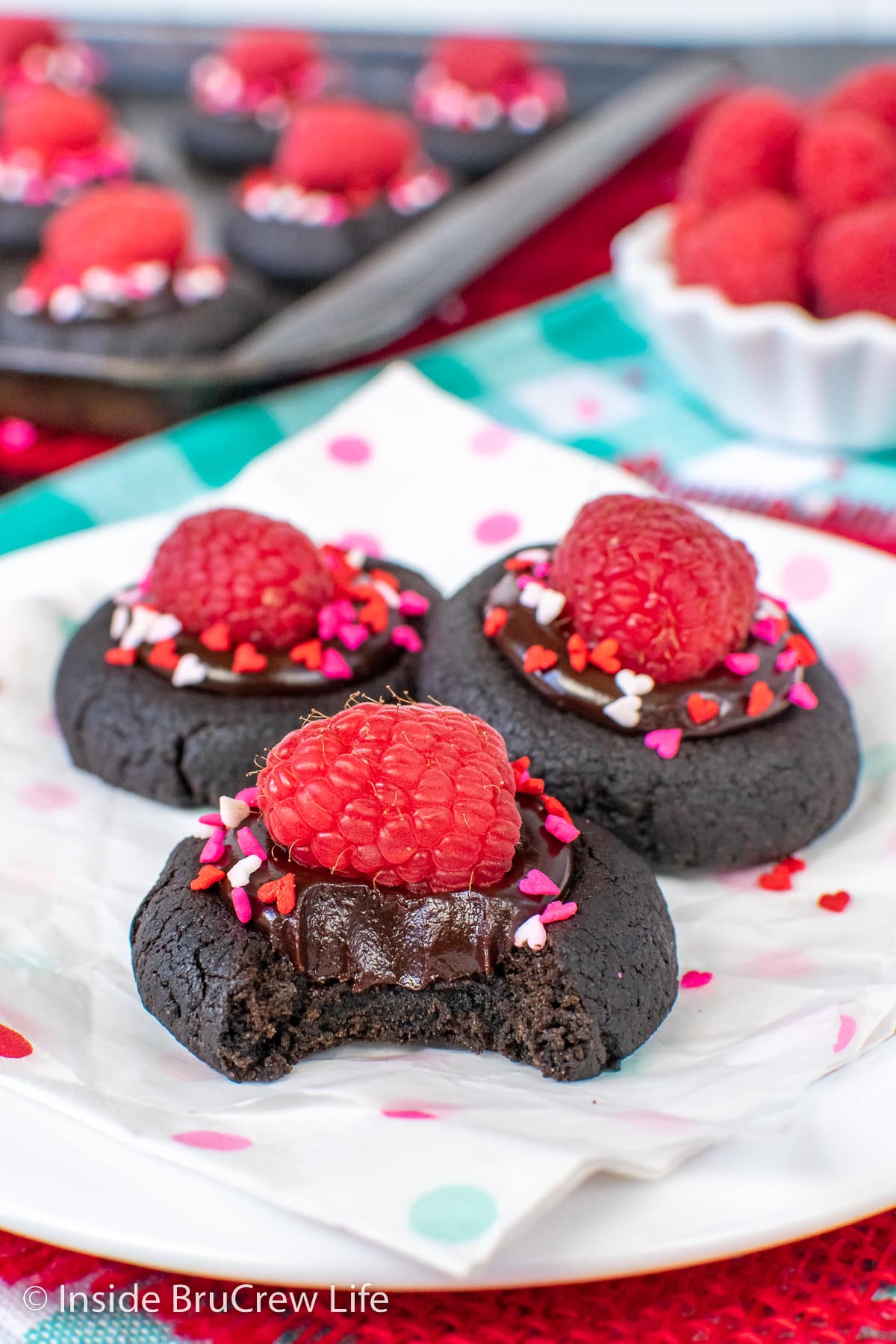 Three chocolate thumbprints topped with raspberries on a white plate.