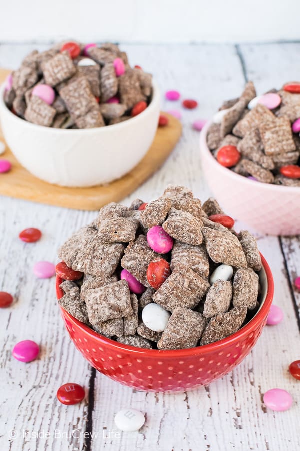 A picture of a red, white, and pink bowls full of M&M's Brownie Batter Muddy Buddies