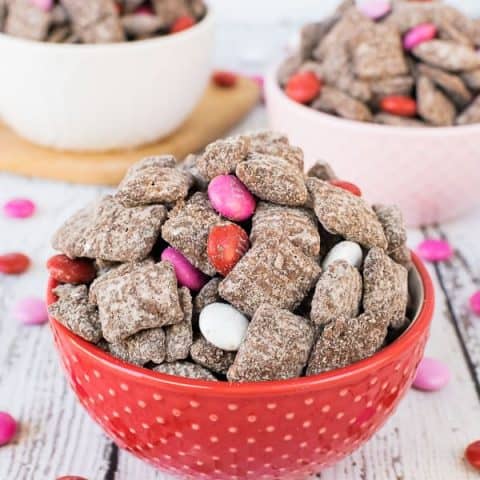 A picture of a red, white, and pink bowls full of M&M's Brownie Batter Muddy Buddies.