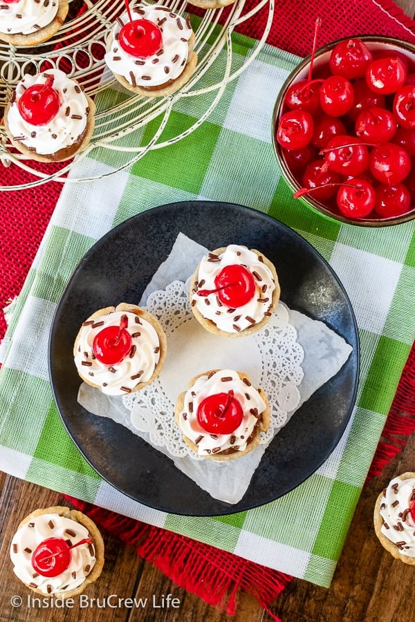 Overhead picture of a black plate with a few chocolate cheesecake bites with Cool Whip and cherries on them.