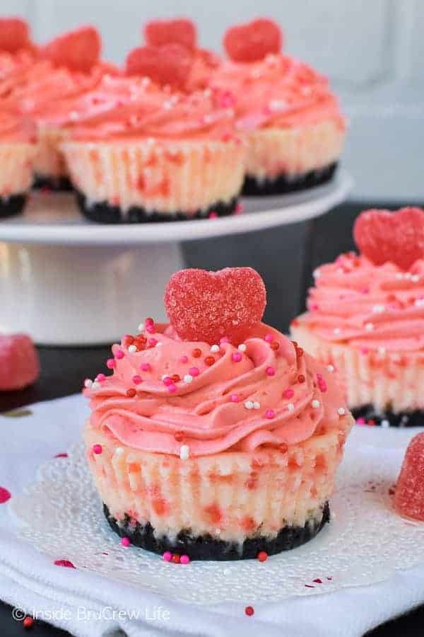 Close up picture of Red Hot White Chocolate Cheesecakes on a white napkin. There is a white cake stand in the background with more cheesecakes. 