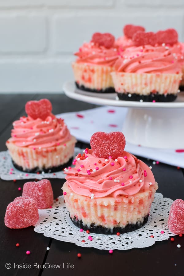 Two Red Hot White Chocolate Cheesecakes on white doilies with a white cake stand behind them with more cheesecakes.