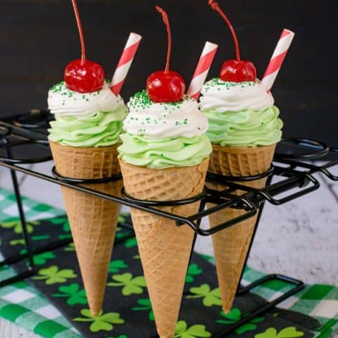 3 ice cream cones filled with green shamrock cheesecake topped with a cherry.