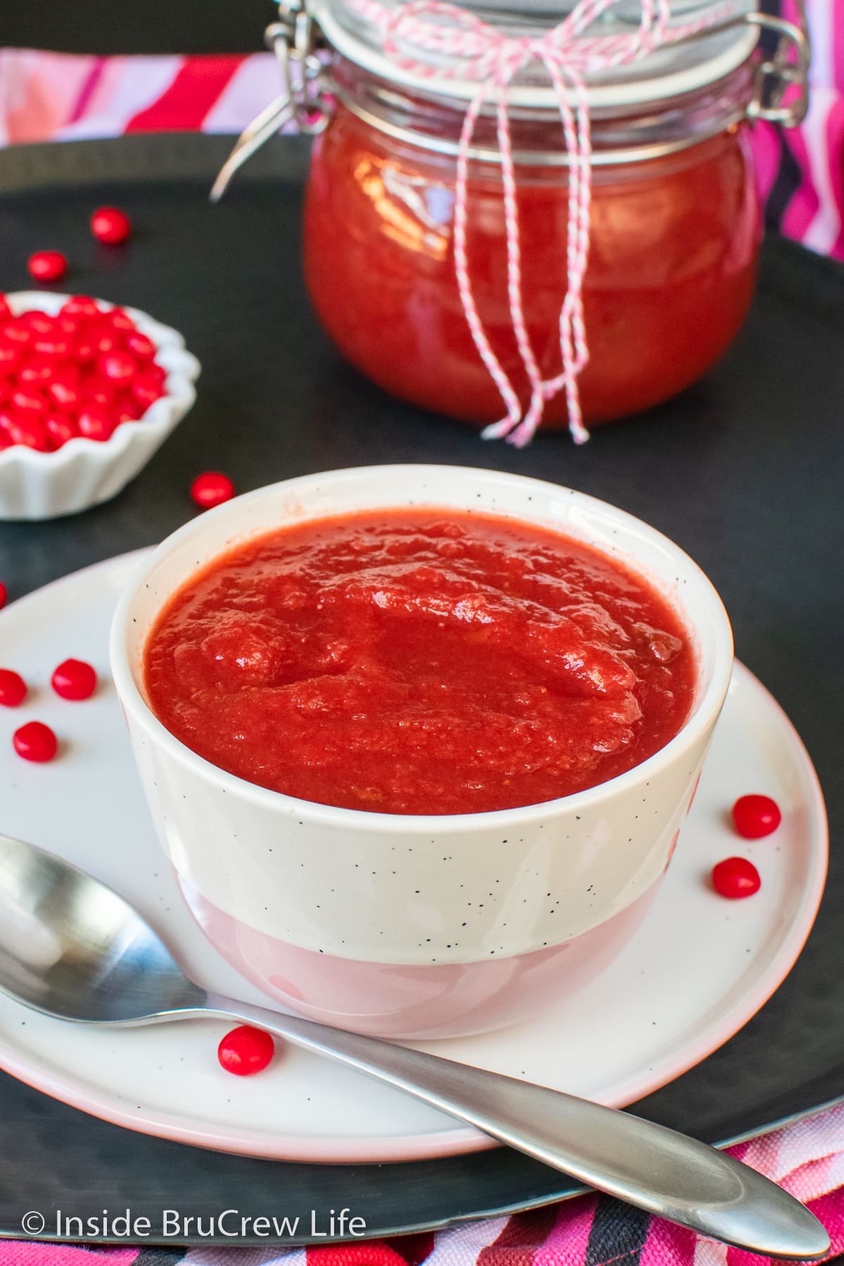  A white bowl filled with red strawberry applesauce.