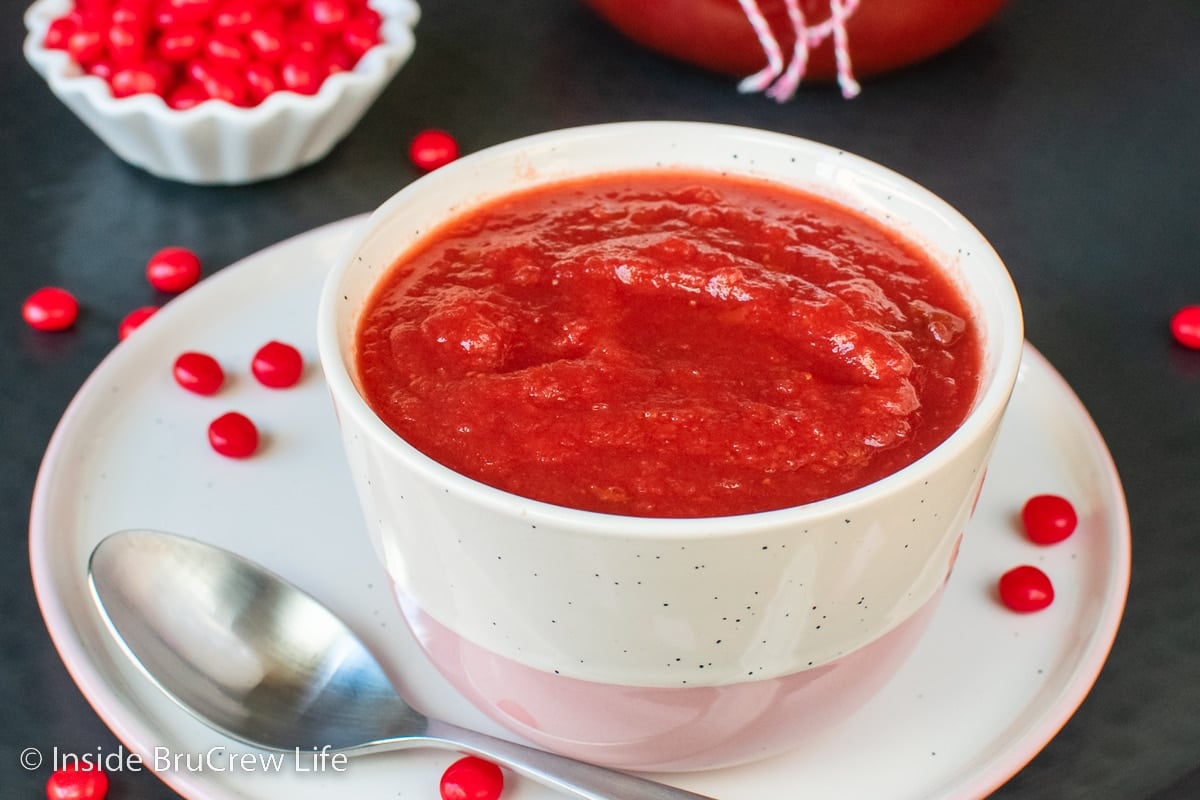 A white bowl filled with red hot applesauce.