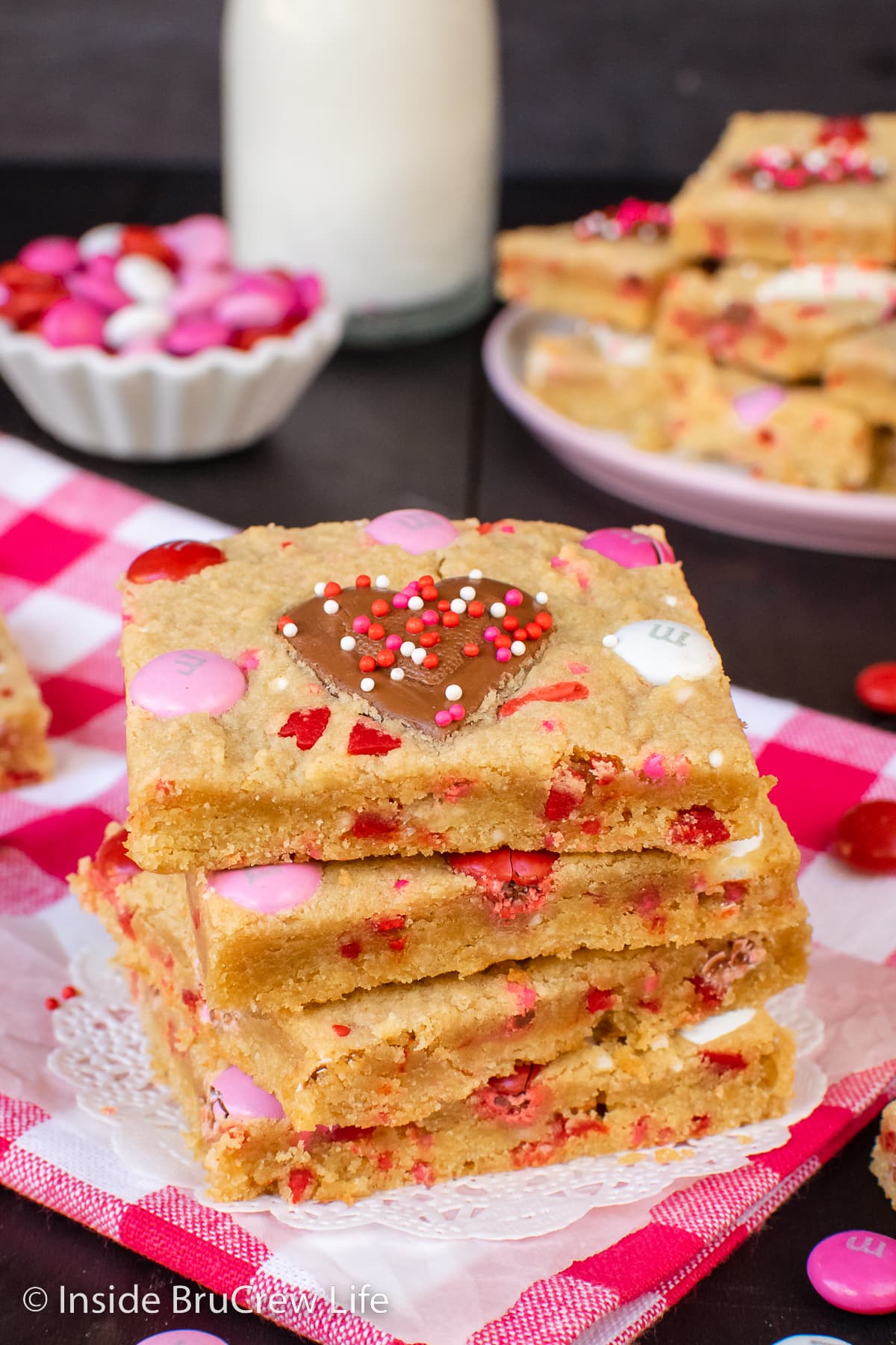 Four peanut butter cookie bars with Reese's hearts stacked on a red and white towel.