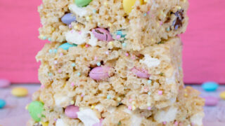 A stack of three Easter rice krispies treats stacked on top of each other with a pink background