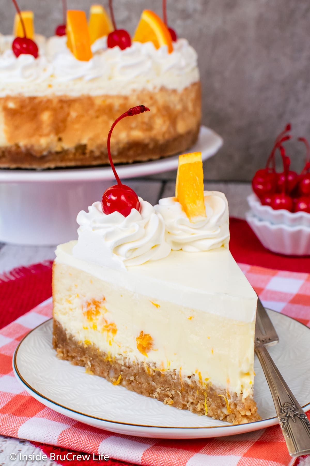 A slice of cheesecake with cool whip, cherries, and oranges.
