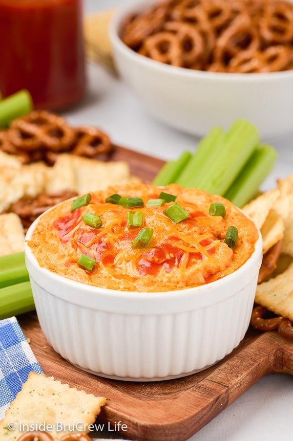 A white bowl on a board filled with cheesy dip.
